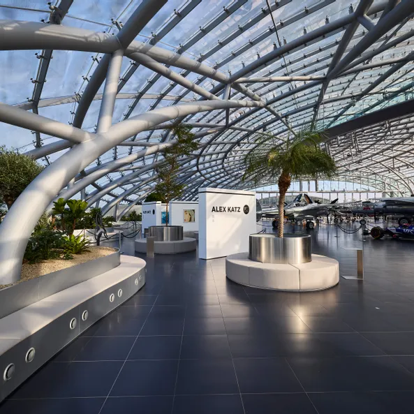 Innenansicht des Hangar-7 mit Glas-Stahl-Architektur,  Sitzgelegenheiten und einer Kunstausstellung.