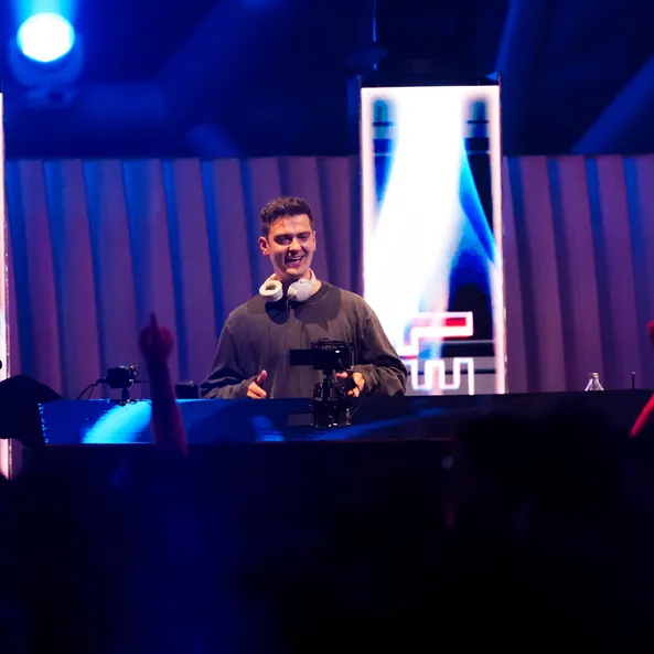Nimino DJ-Set beim Sunset-Event im Hangar-7 – der Künstler lächelt hinter dem Pult vor blau illuminiertem Hintergrund und feierndem Publikum.